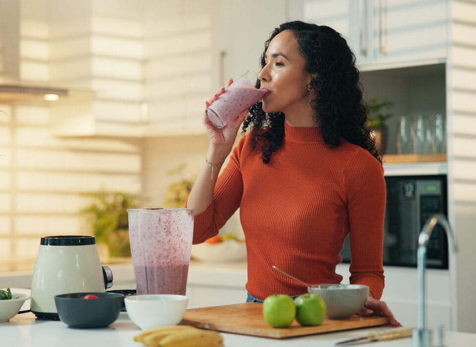 Donna che beve un frullato proteico in cucina