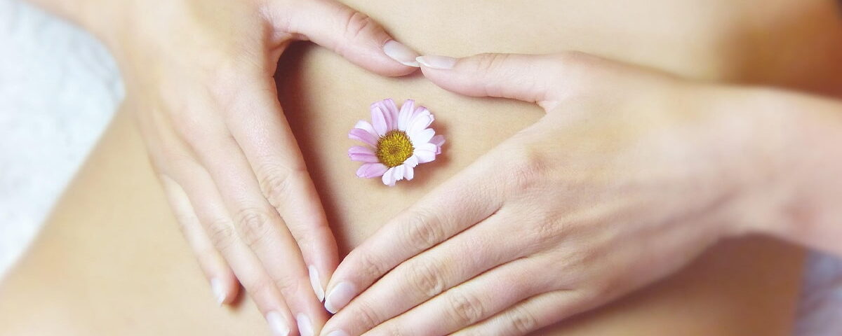 Mani di una donna posizionate a forma di cuore sull'addome, con un piccolo fiore al centro